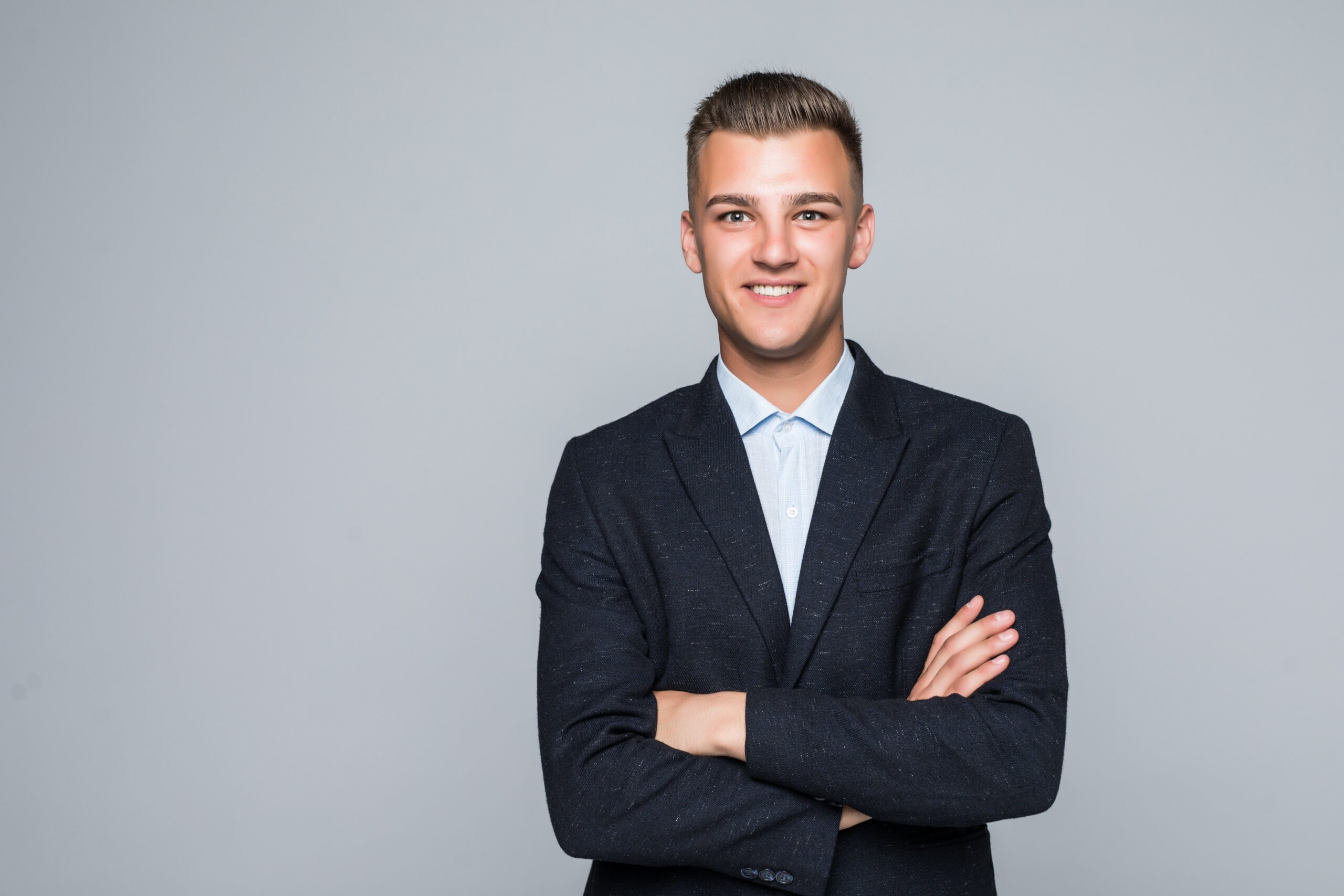 beautiful young man student businessman jacket holds his arms crossed isolated light grey wall min scaled