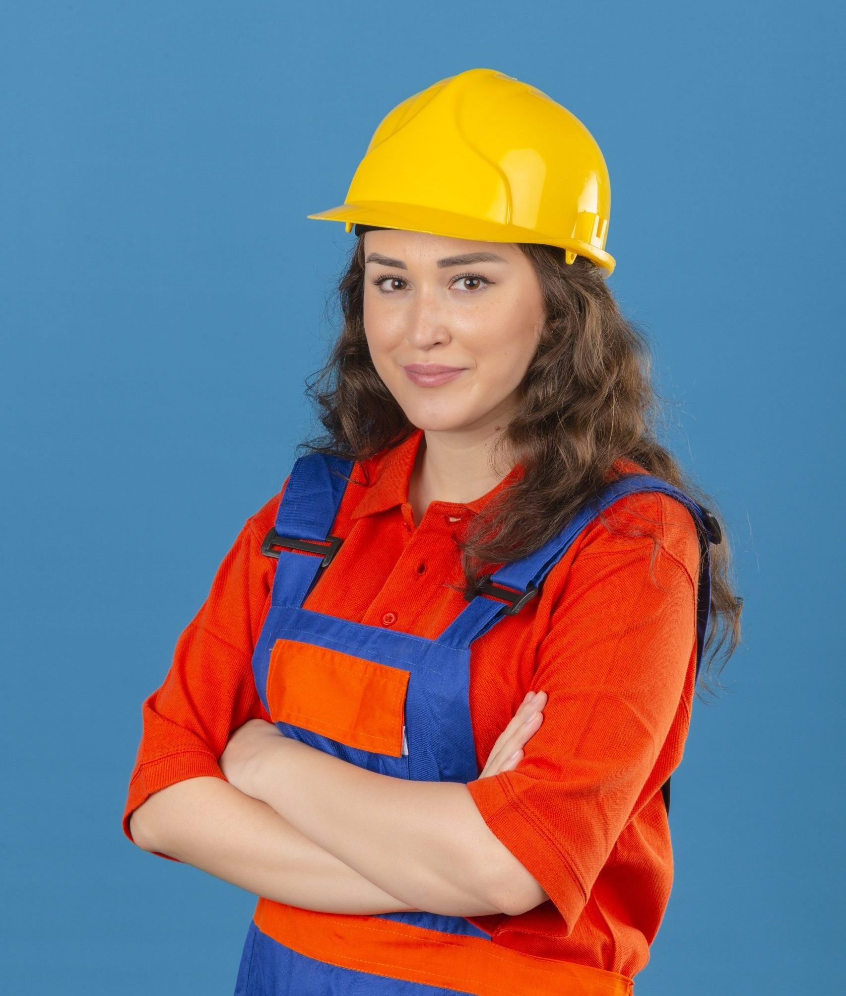 young builder woman construction uniform safety helmet standing with crossed arms chest looking confident happy isolated blue wall1 scaled e1700259757987